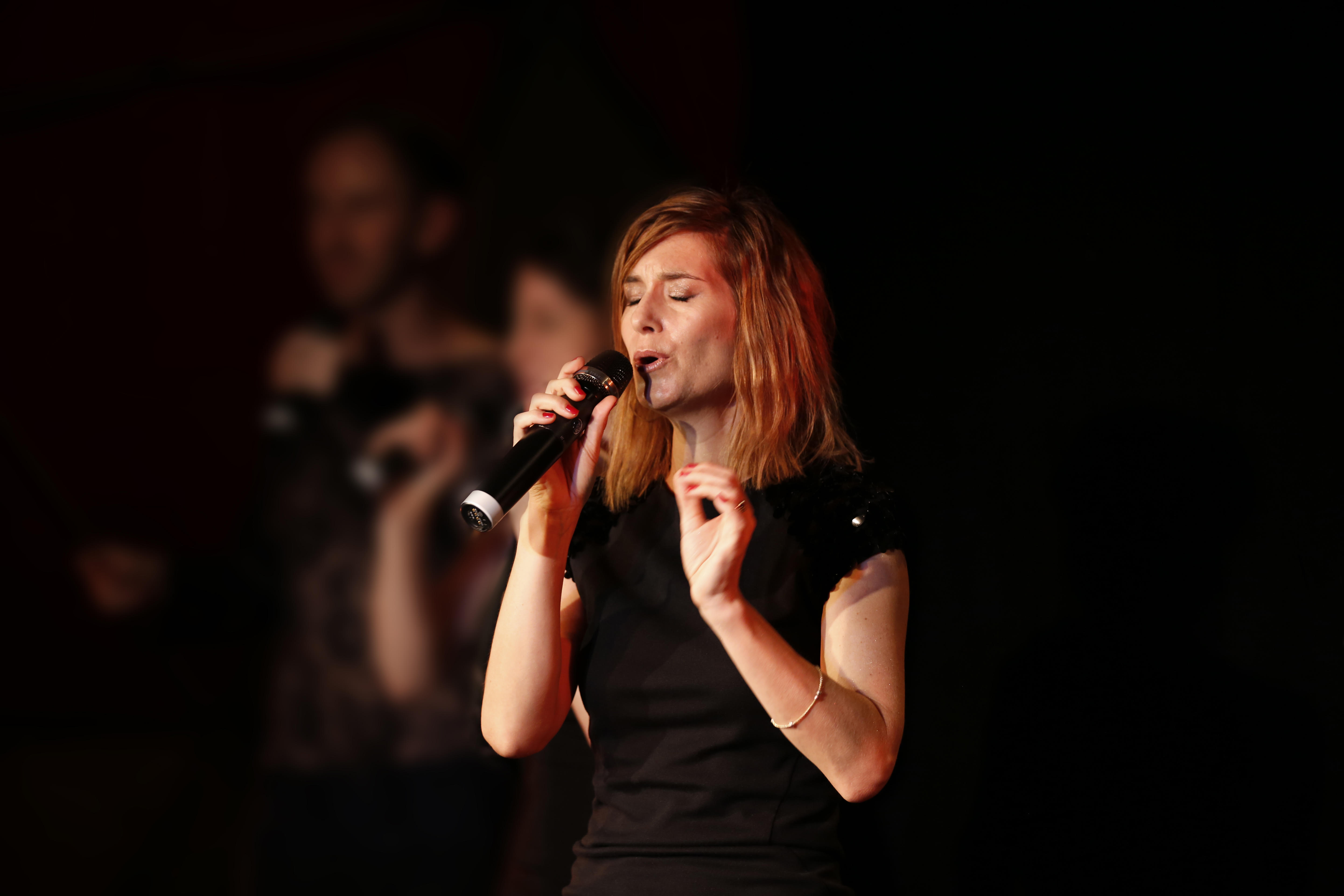 Woman holding a microphone and singing, with eyes closed