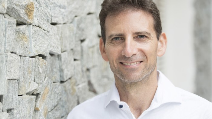 Headshot of Serge Benhayon leaning against a brick wall