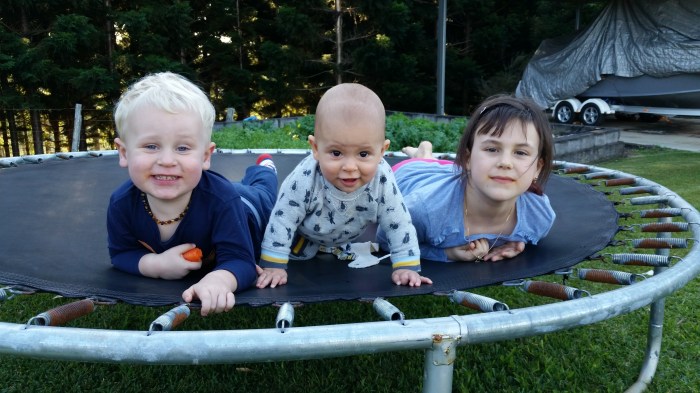 3 young children smiling as they all look ahead laying on a trampoline