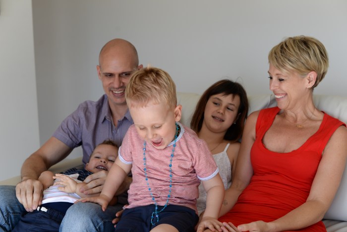 Nicole Serafin sitting on the couch laughing and being playful with her partner and 3 children